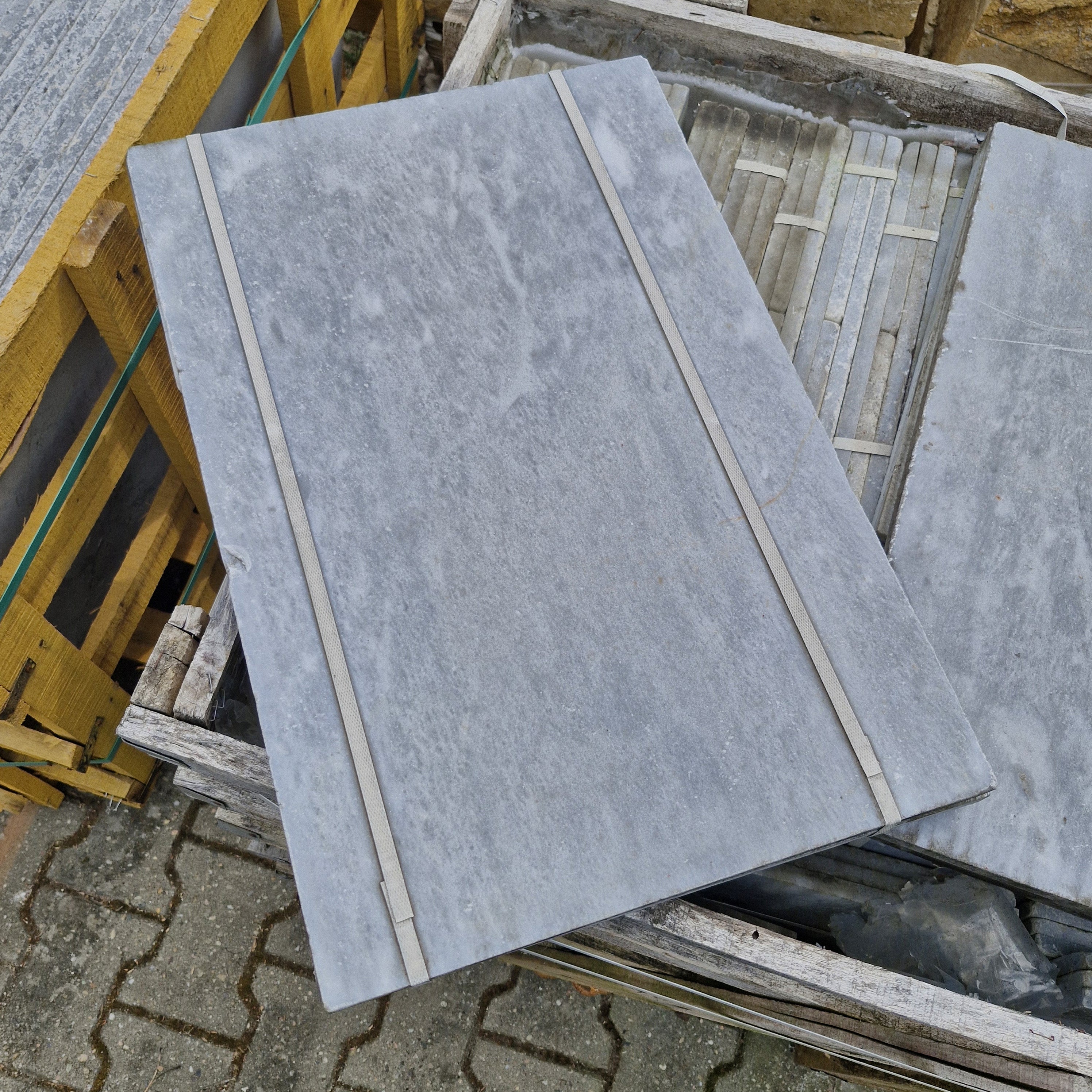Helle getrommelte Marmorfliesen von CAMELIA, Naturstein, quadratisch, Oberfläche mit natürlicher Maserung, liegend auf einem Boden.